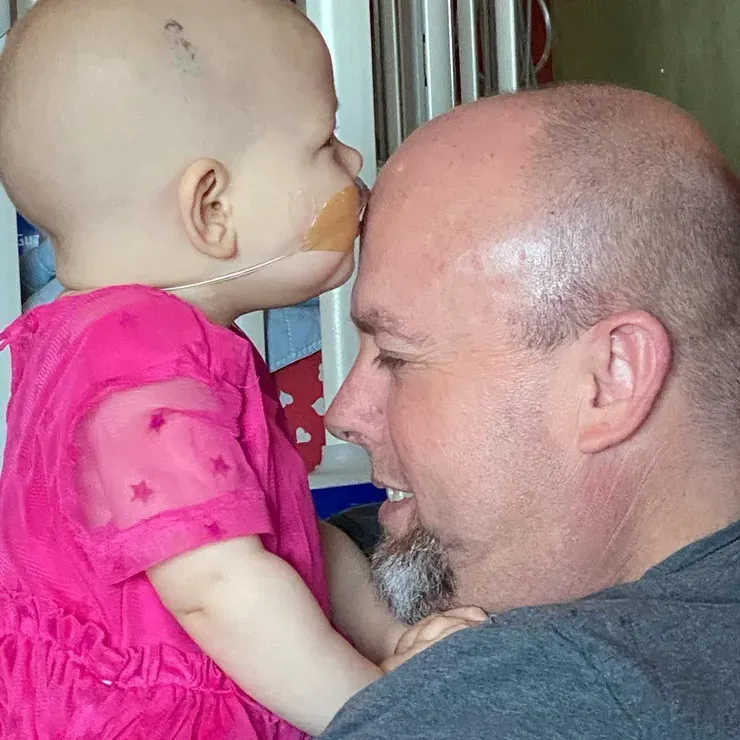 Jazmine in a pink dress, nose to nose with her dad, both smiling.