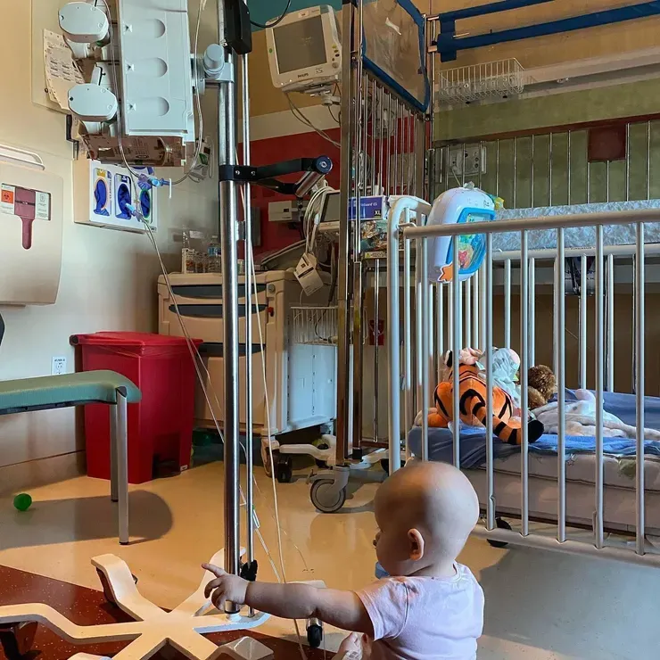 Jazmine pointing across her hospital room, her world made cozy with toys and blankets.