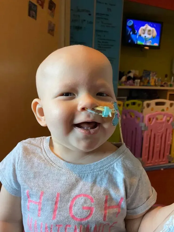 Jazmine laughing with her whole face, a feeding tube taped to her cheek with a cheerful sticker.